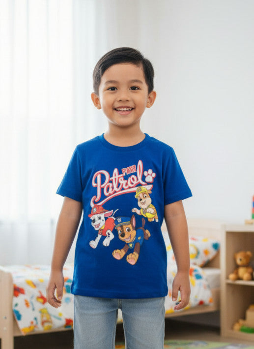 Child wearing a blue 'Patrol' t-shirt in a room with colorful bedding.