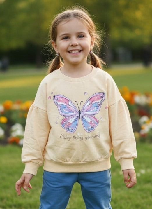 Young girl wearing a beige sweatshirt with a butterfly design outdoors.